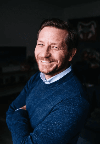 Kaleeg Hainsworth, founder of Kaos Intelligence, smiling in a navy sweater